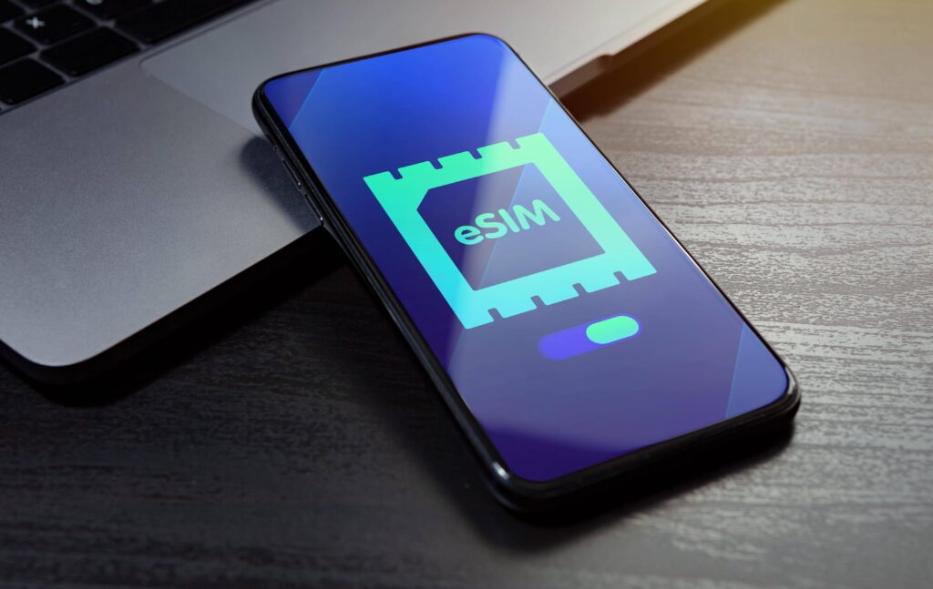 Smartphone showing eSIM activation screen next to a laptop on wooden desk