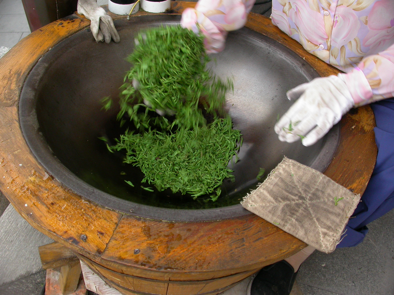Hand frying West Lake Longjing tea leaves in a heated iron wok by tea master