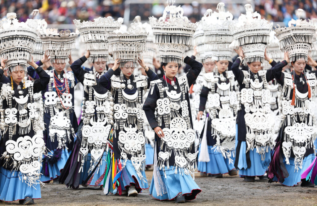 Yi ethnic minority women wearing elaborate silver headdresses and traditional blue pleated skirts performing a ceremonial dance at Yi Torch Festival in Yunnan