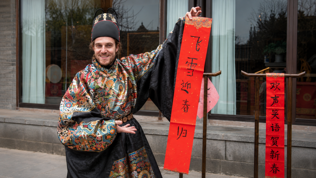 Foreign man in colorful Ming dynasty style hanfu holding a red Chinese New Year spring couplet banner