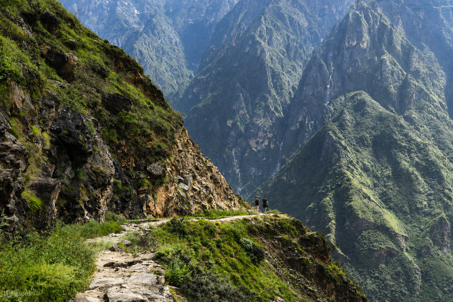 Two hikers on the Tiger Leaping Gorge high trail with deep canyon walls and green mountain ridges