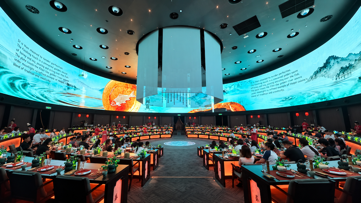 Guests in traditional Chinese robes dining at the Shanghai immersive dinner show while performers dance on the rotating stage